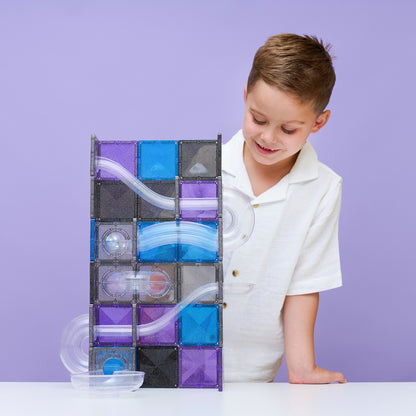 Kind bouwt een Connetix Ball Run Galaxy Pack met transparante glittertegels en knikkerbaanonderdelen