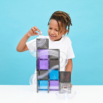 Kind bouwt een Connetix Ball Run Galaxy Pack met transparante glittertegels en knikkerbaanonderdelen